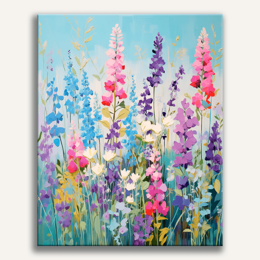 A vibrant canvas print displaying a colorful wildflower field with tall stems and various shades of pink, purple, red, and white flowers, set against a bright blue sky with scattered clouds..